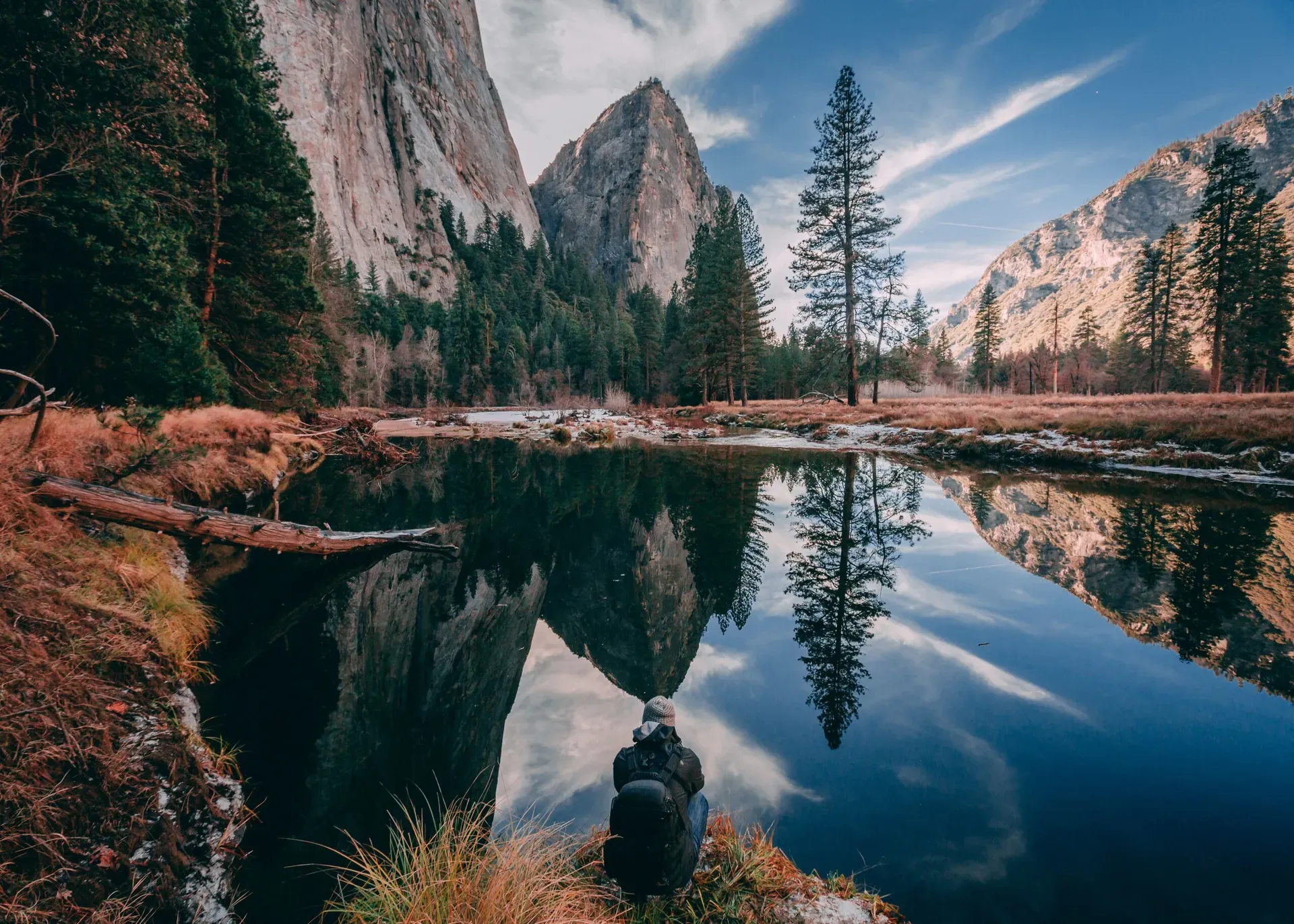 Hiker viewing granite cliffs reflected in calm river waters