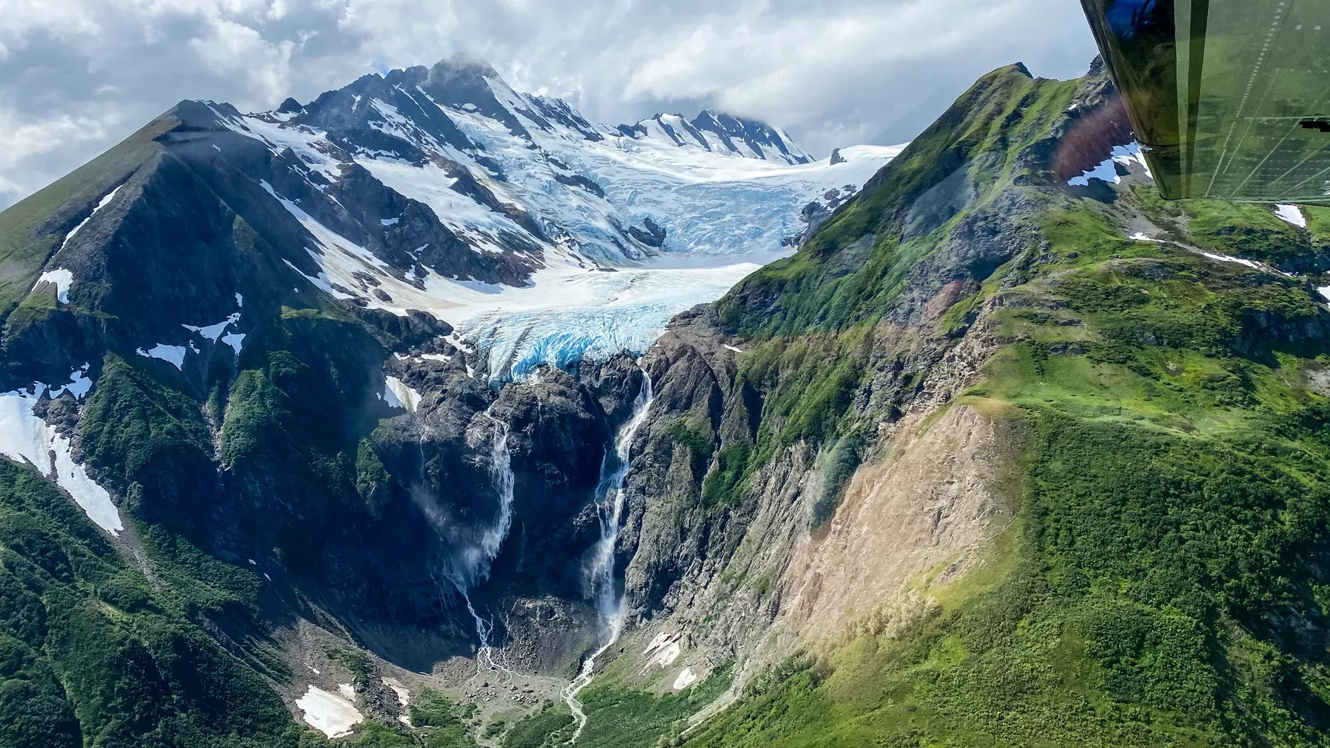 Massive tidewater glacier with waterfalls cascading into green valleys