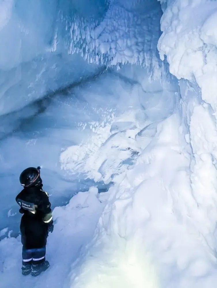 Solo explorer wearing helmet and winter gear standing inside a deep blue glacial cavern
