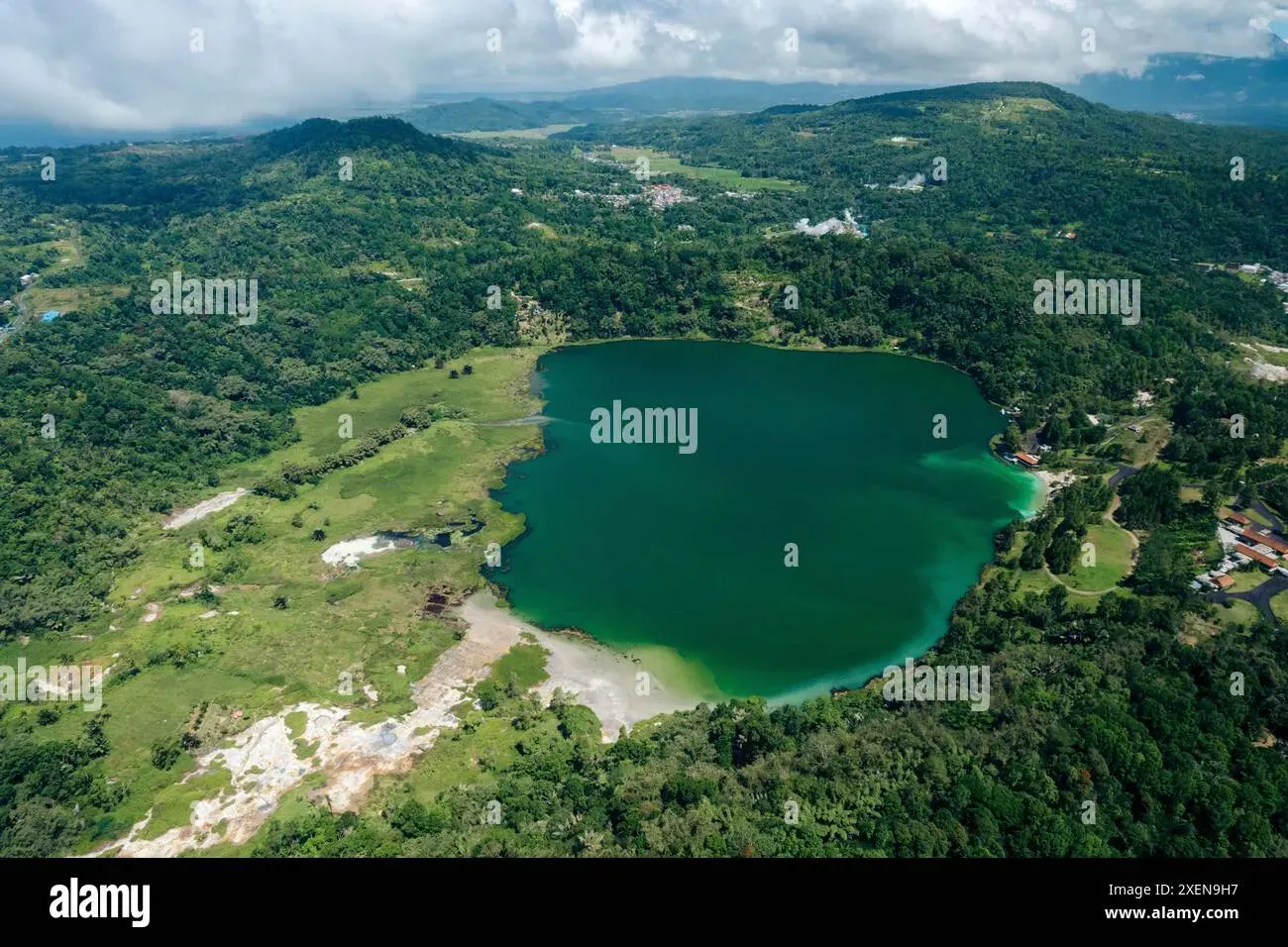 Aerial perspective of Lake Linow's green sulfurous crater lake with surrounding hills