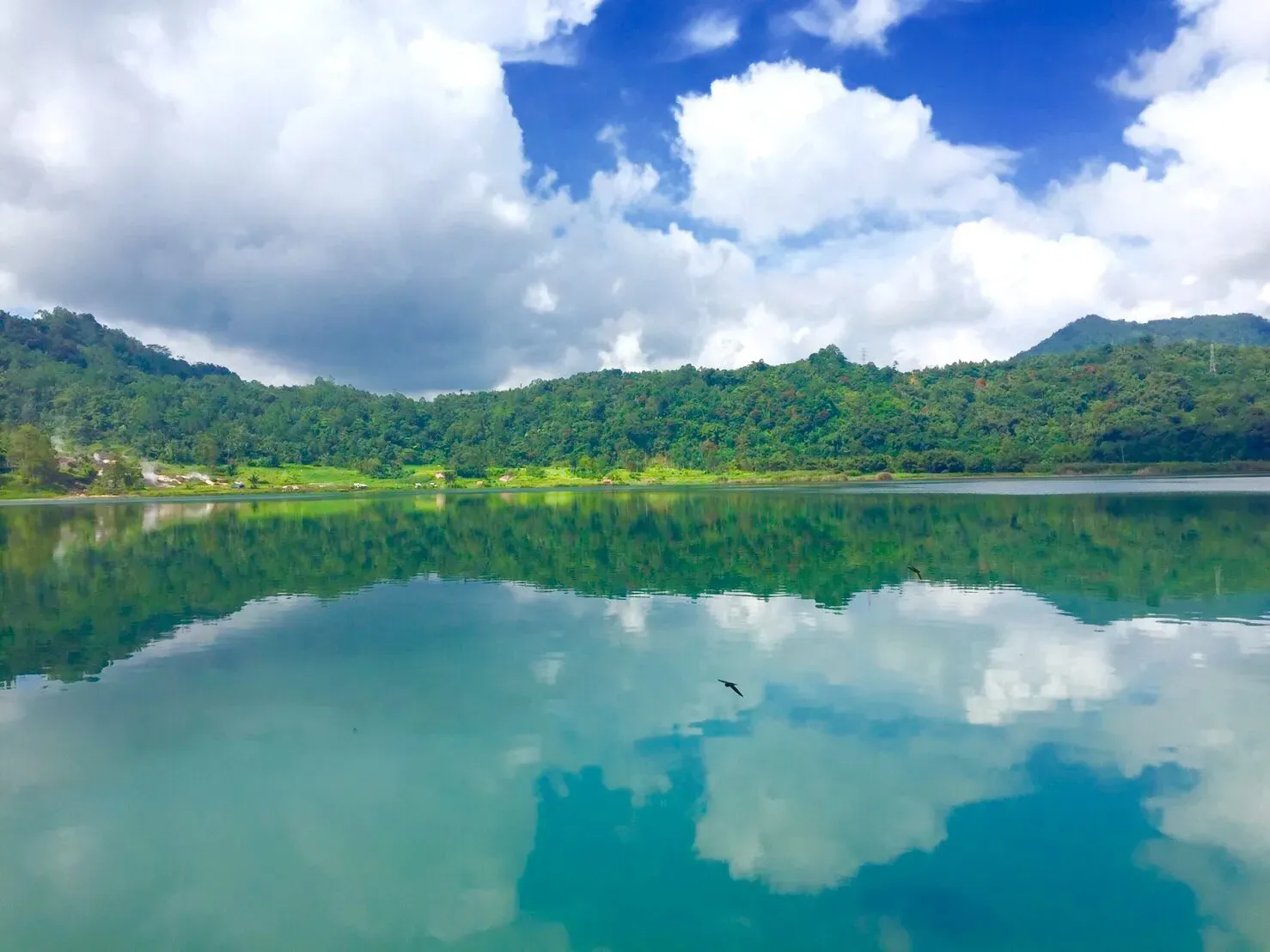 Calm reflective green waters of Lake Linow surrounded by lush tropical hills