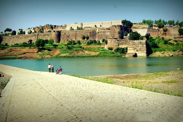 Gagron Fort with a serene water body in the foreground and a curved stone pathway leading to the historic gates