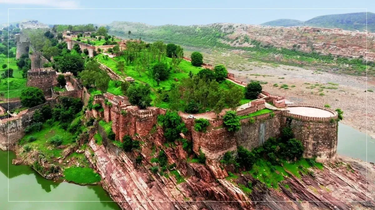 Red sandstone walls and bastions of Gagron Fort standing atop rocky cliffs overlooking lush greenery and water