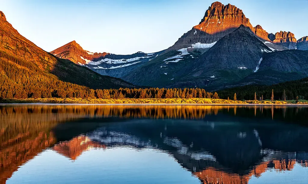 Golden sunrise light over Swiftcurrent Lake in Many Glacier area with mountain peaks in background