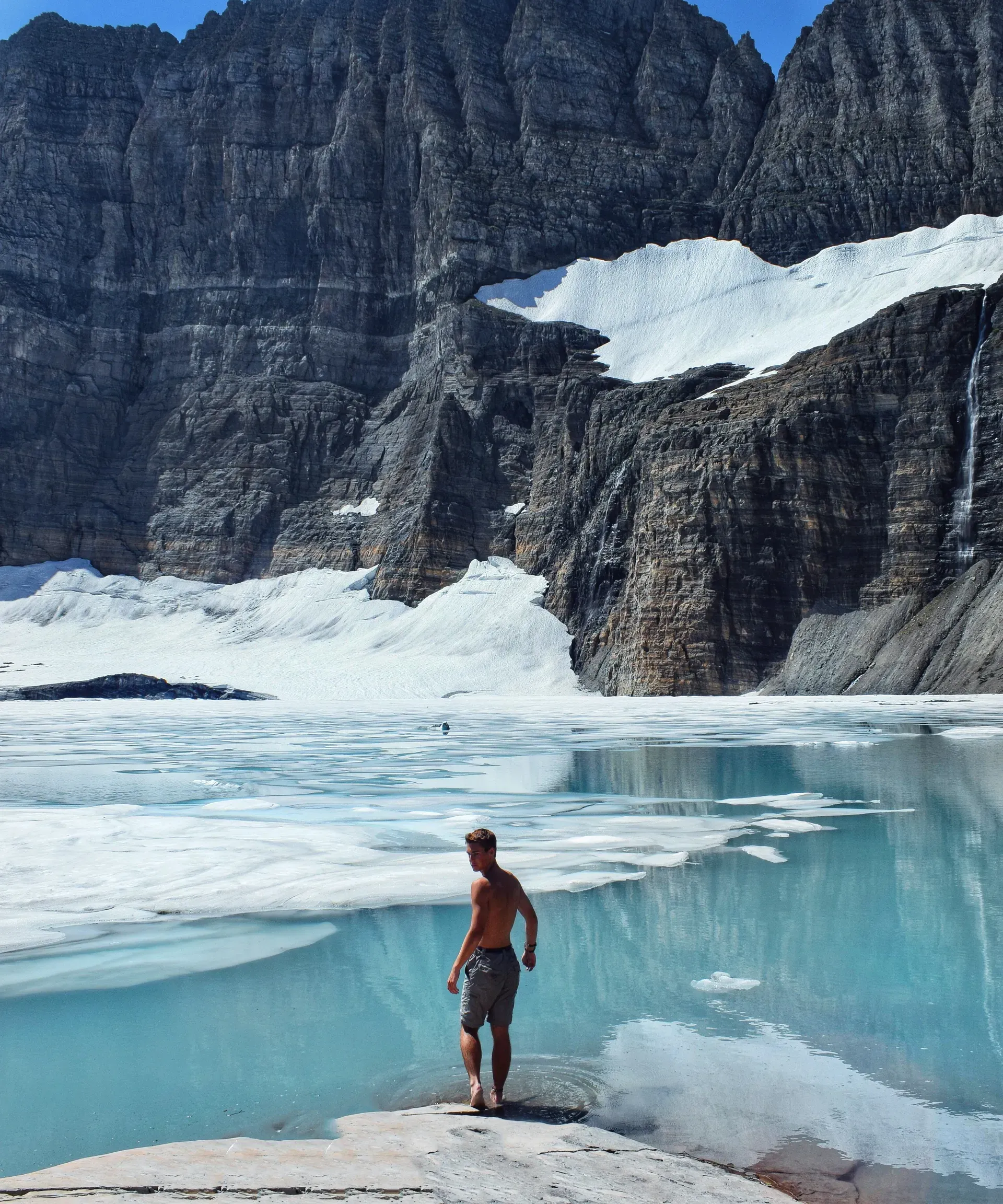 Hiker standing on overlook admiring turquoise glacial lake surrounded by snow-capped mountains