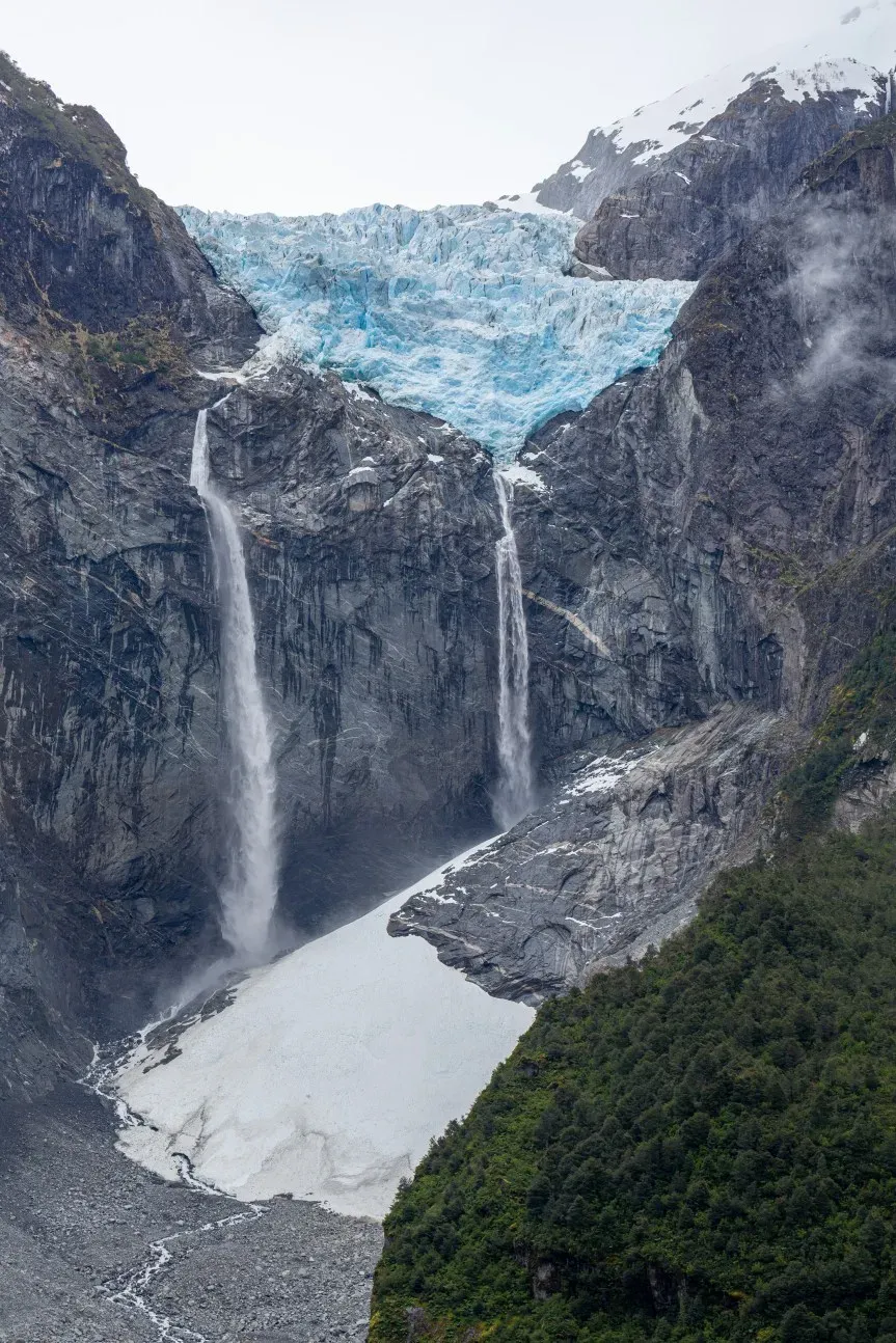 Massive hanging glacier feeding two powerful waterfalls cascading down dark cliffs