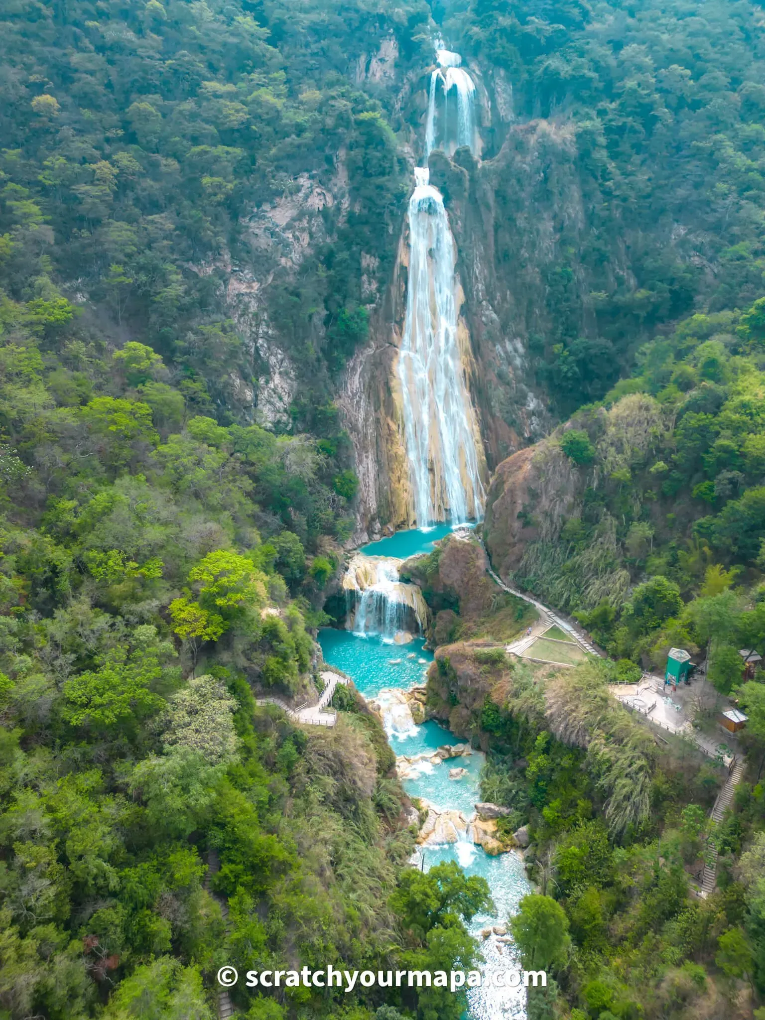 Multi-tiered turquoise waterfall cascading down lush green mountainside