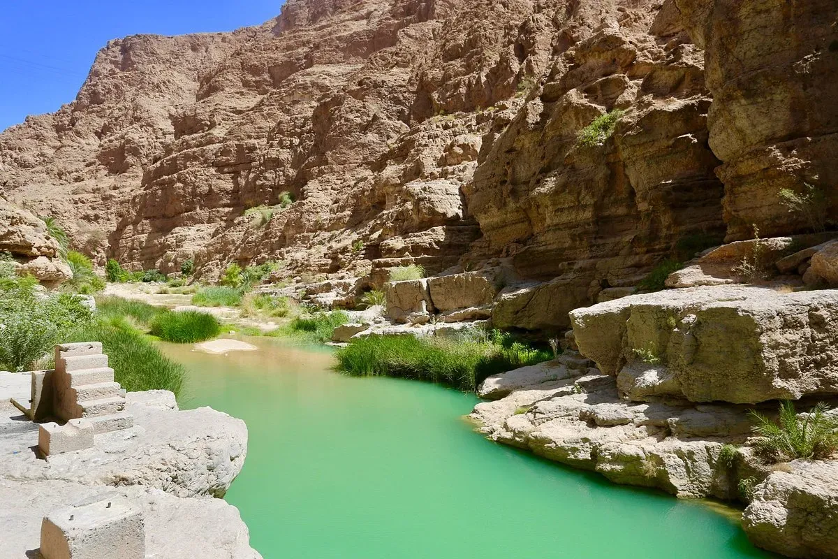 Narrow green river with stone steps in Wadi Shab
