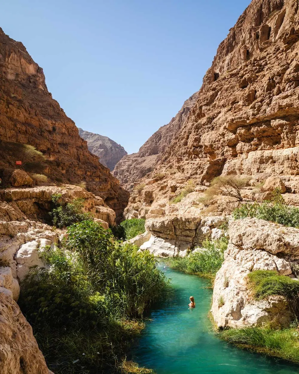 Person swimming through narrow turquoise water channel in Wadi Shab Oman
