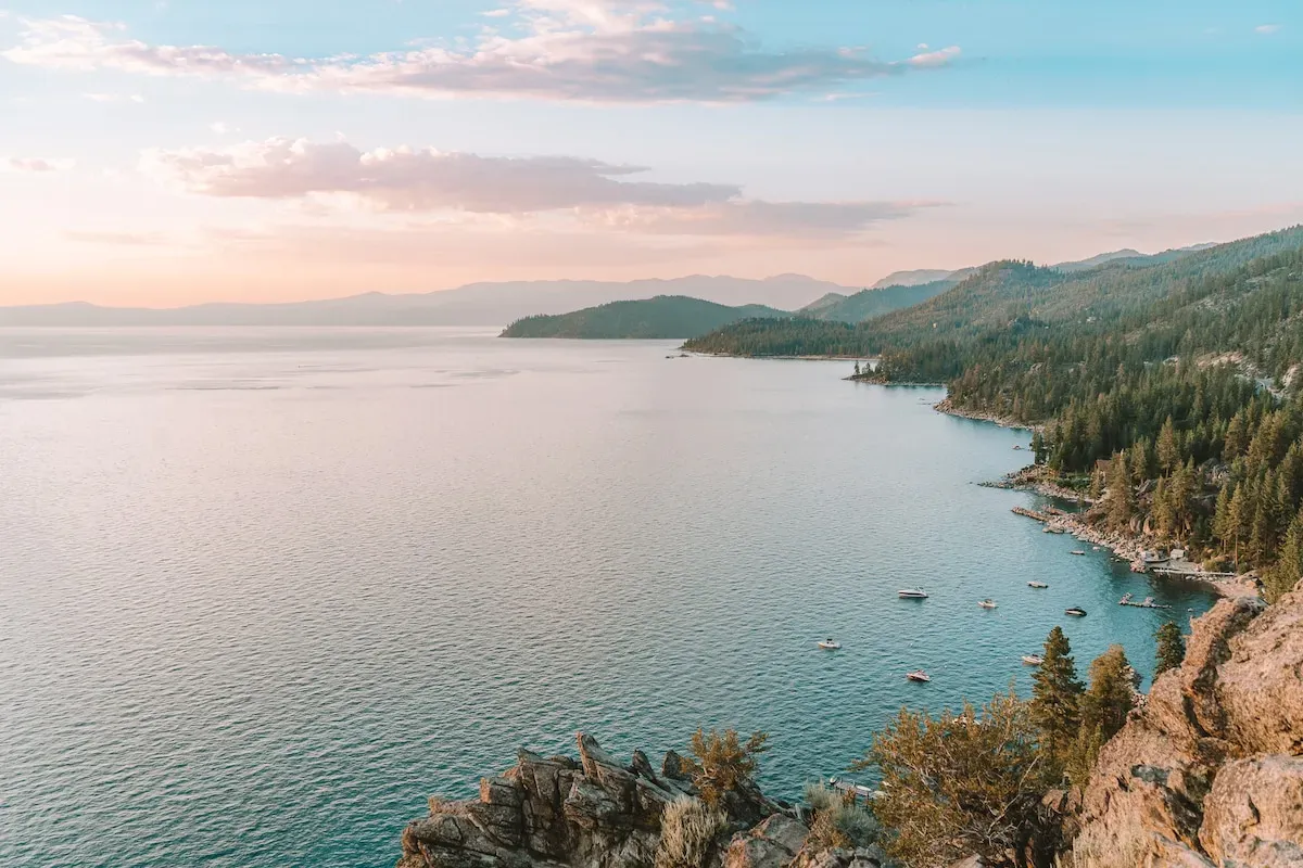 Serene view of Lake Tahoe with calm clear waters, pine-covered mountains, and boats anchored near the shore