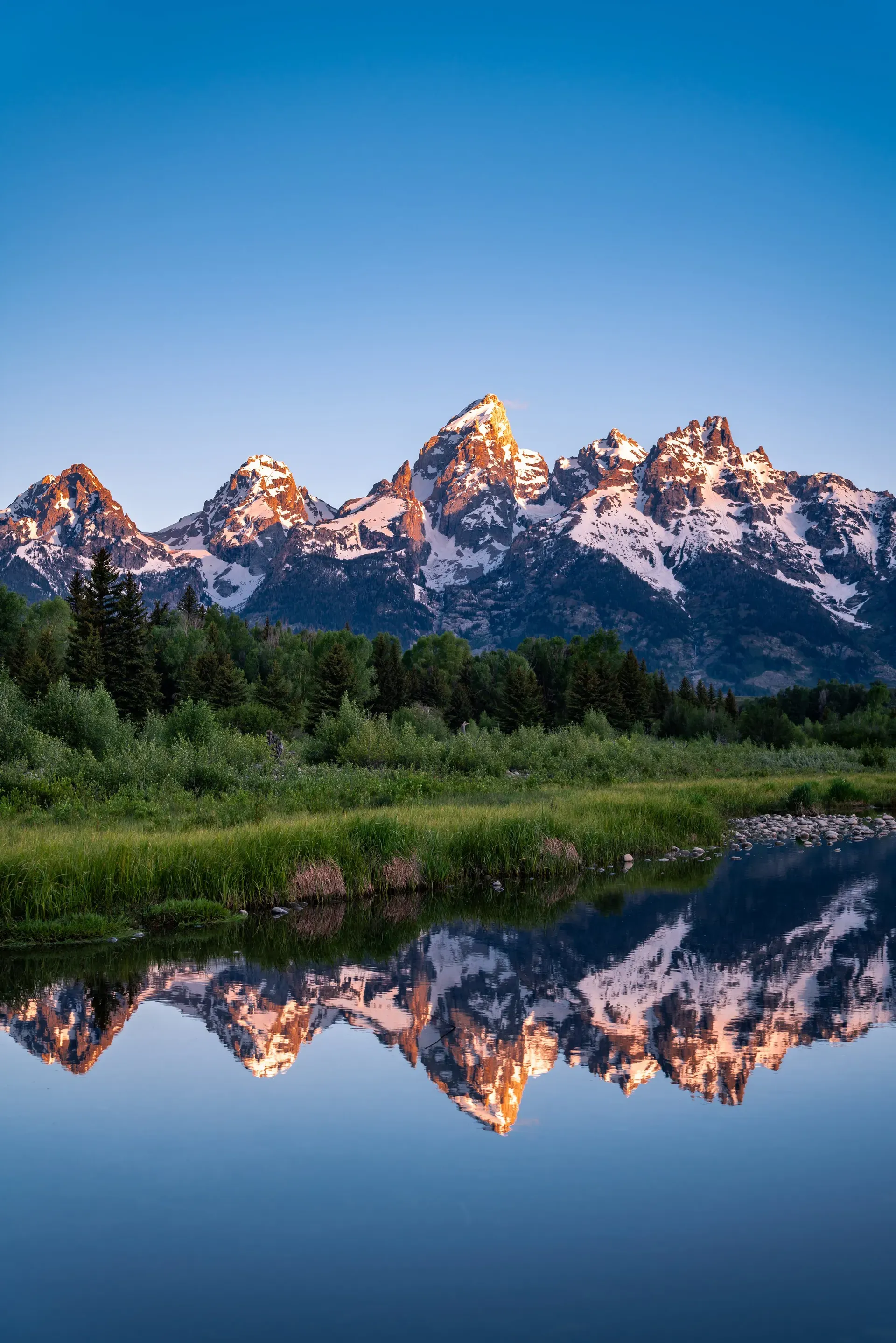 Snow-capped Grand Teton peaks at sunset reflected in the Snake River