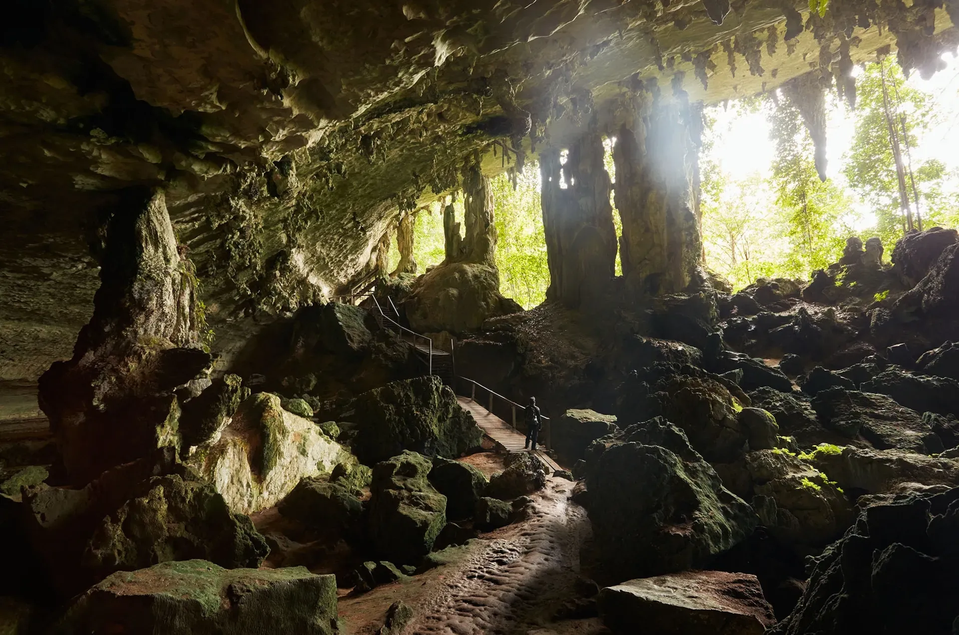 Sunlight streaming into Niah Caves Malaysia illuminating visitors on wooden walkway