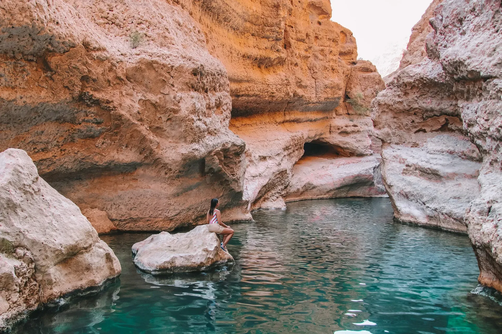 Tranquil turquoise pool surrounded by reddish-orange rock in Wadi Shab Oman