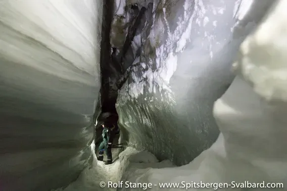 Travelers navigating a narrow icy passage inside the Longyearbreen ice cave