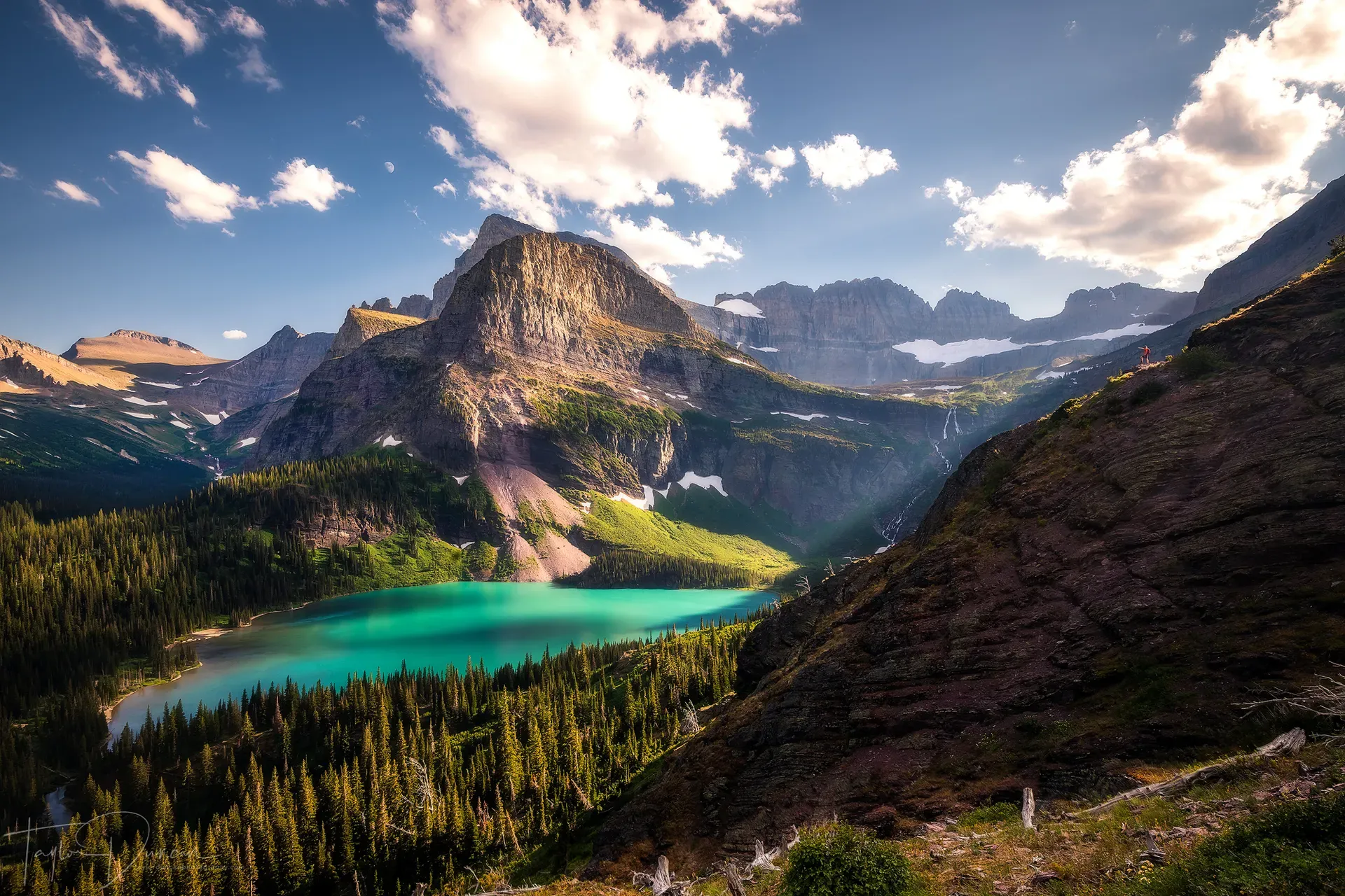 Turquoise waters of Grinnell Lake surrounded by evergreen forests and towering rugged peaks