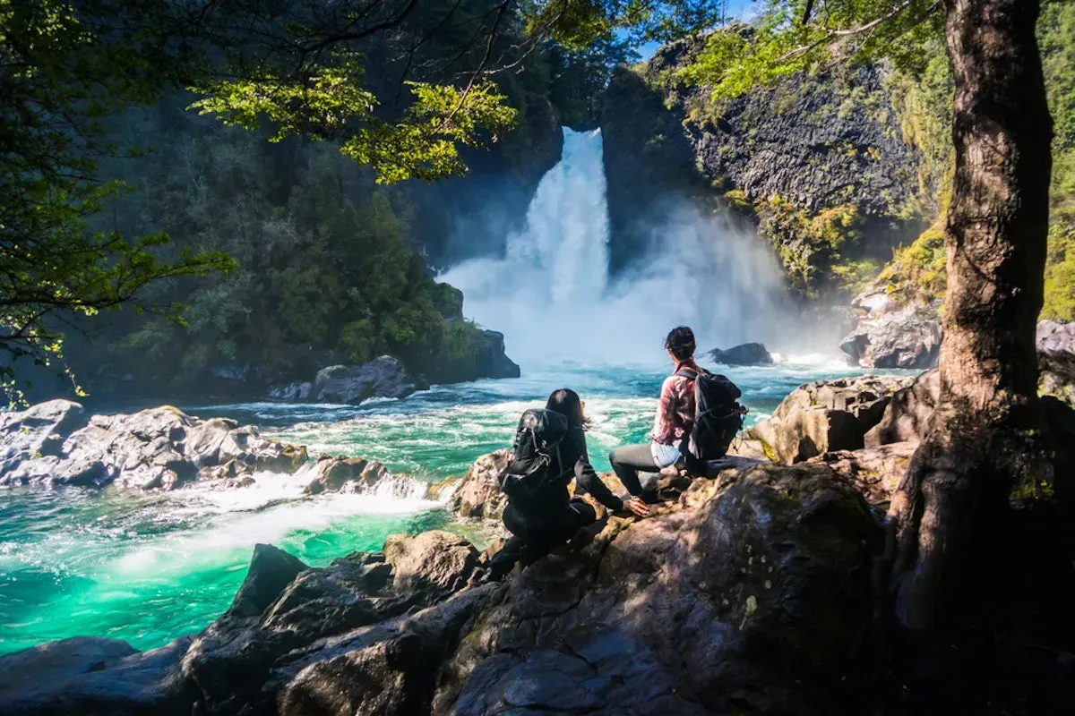 Hikers admiring a waterfall by a turquoise river