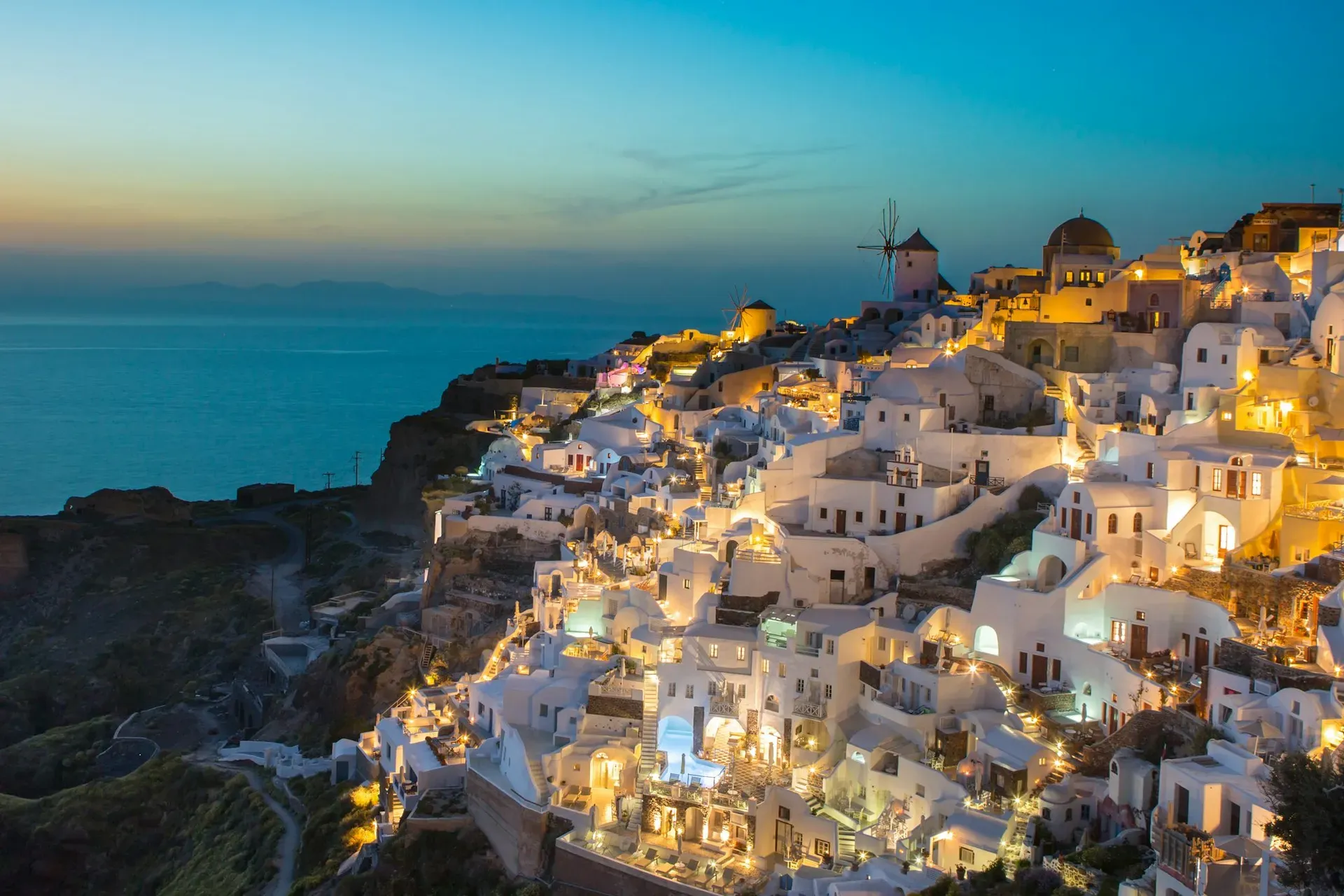 White Cycladic houses built into cliffside above blue sea