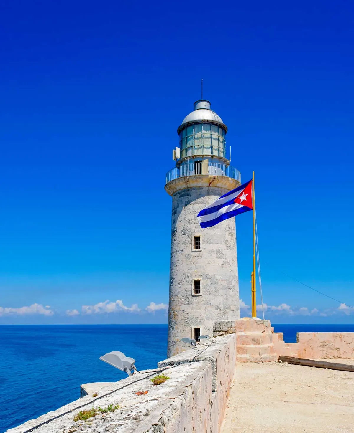 White lighthouse at Castillo del Morro with Cuban flag flying against a bright blue sky