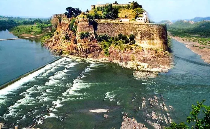 Wide landscape of Gagron Fort overlooking a river with a dam, lush green hills, and open blue sky
