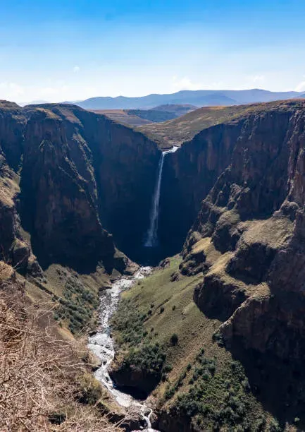 A hiker standing on the edge of a cliff overlooking Boalathapo Falls plunging into a deep canyon in Lesotho