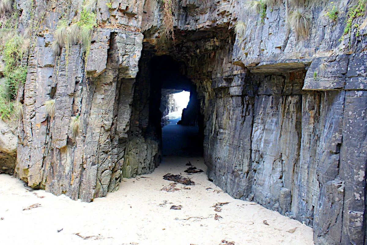 A narrow rock passageway leads into the opening of Remarkable Cave Tasmania with sandy ground and sparkling water