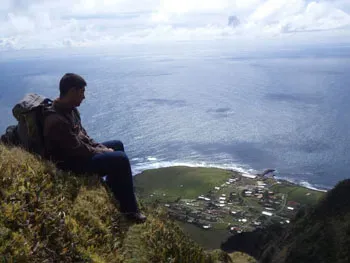 A person sitting on a grassy slope overlooking the settlement of Edinburgh of the Seven Seas with Queen Mary's Peak in the background