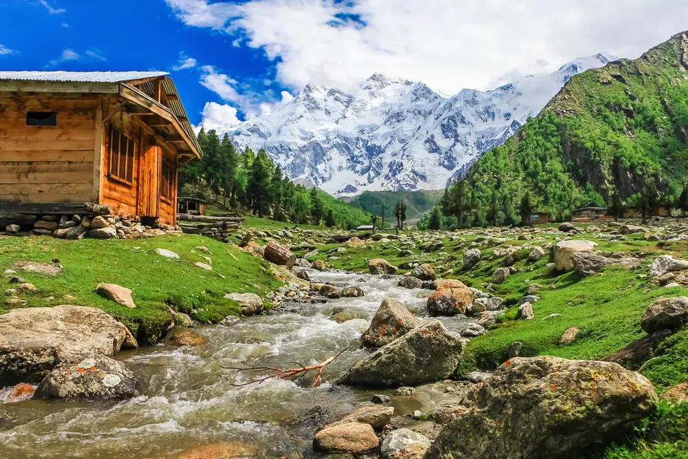 Wooden cabin beside rushing stream with Nanga Parbat in background