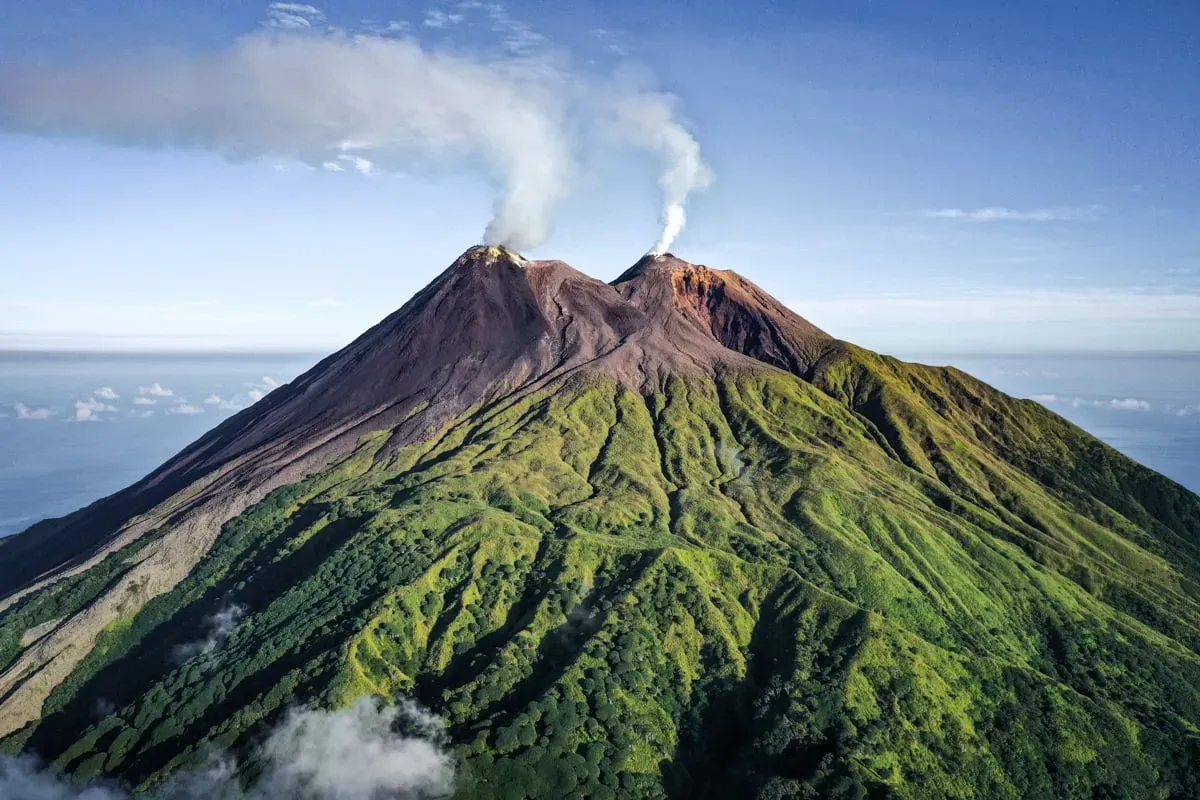 Aerial drone photo of Mount Karangetang's twin smoking craters on a lush green volcanic cone on Siau Island, North Sulawesi, Indonesia