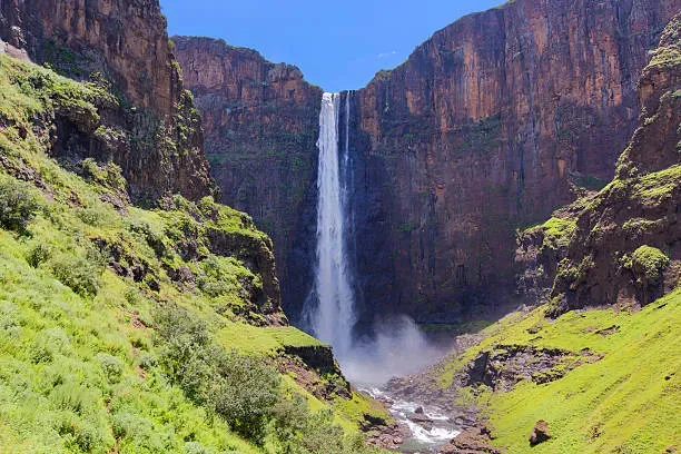Boalathapo Falls plunging down a cliff into a lush green valley surrounded by reddish-brown rock formations in Lesotho