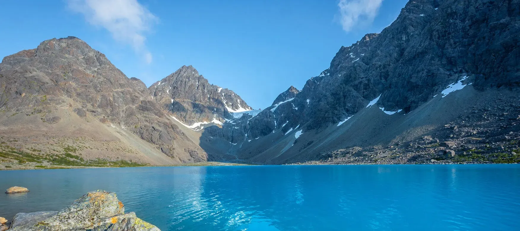 Bright turquoise glacial lake Blåisvatnet Norway surrounded by rocky terrain and snow-capped mountains under overcast sky