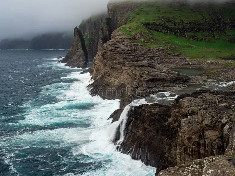 Bøsdalafossur waterfall on Vágar with green cliffs and crashing ocean waves