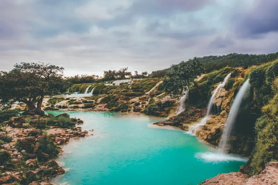 Cascading Darbat Steps Waterfall flowing into a turquoise pool under cloudy skies, Dhofar Oman