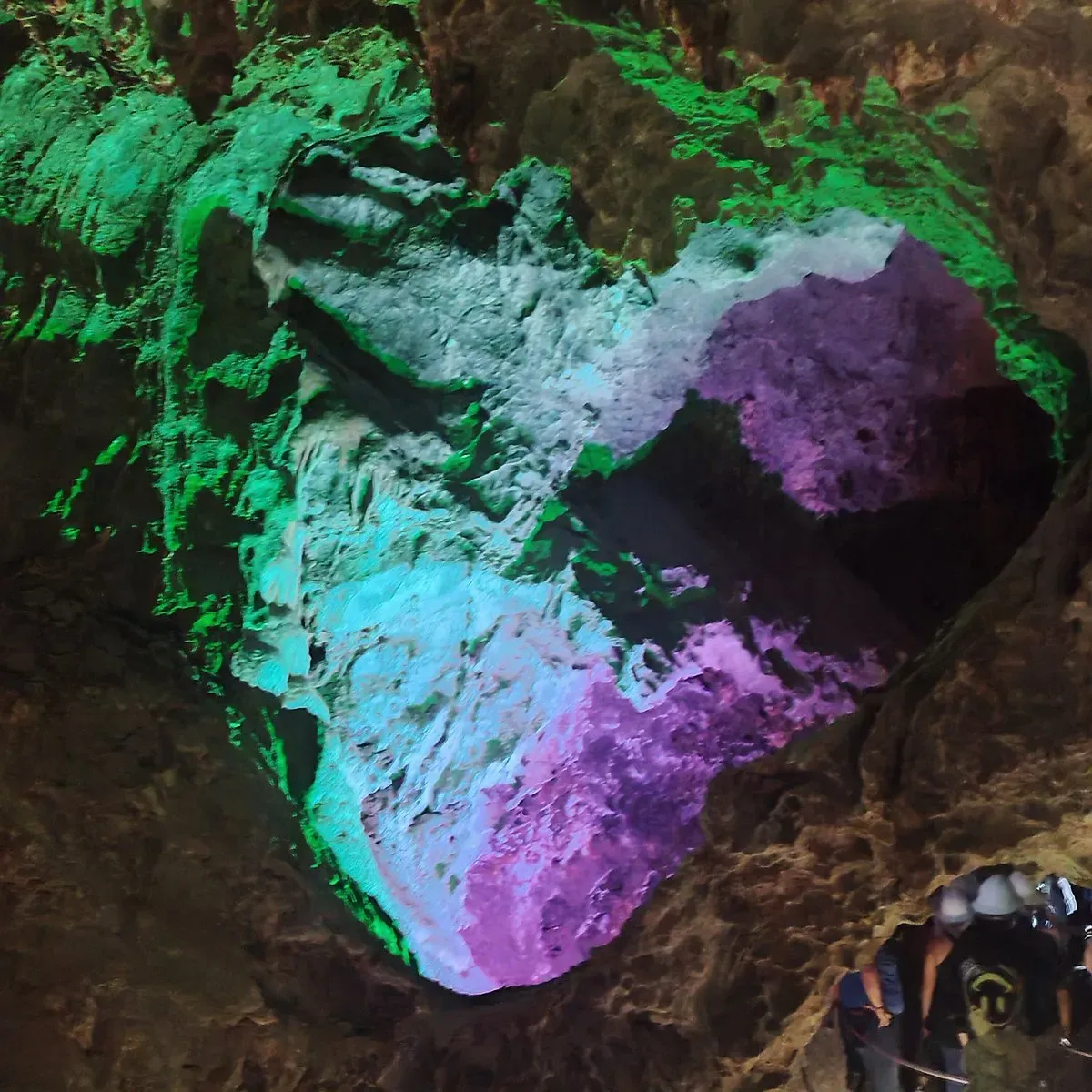 Cavers exploring illuminated rock formations inside Grutas de Nombre de Dios Chihuahua with colorful lighting