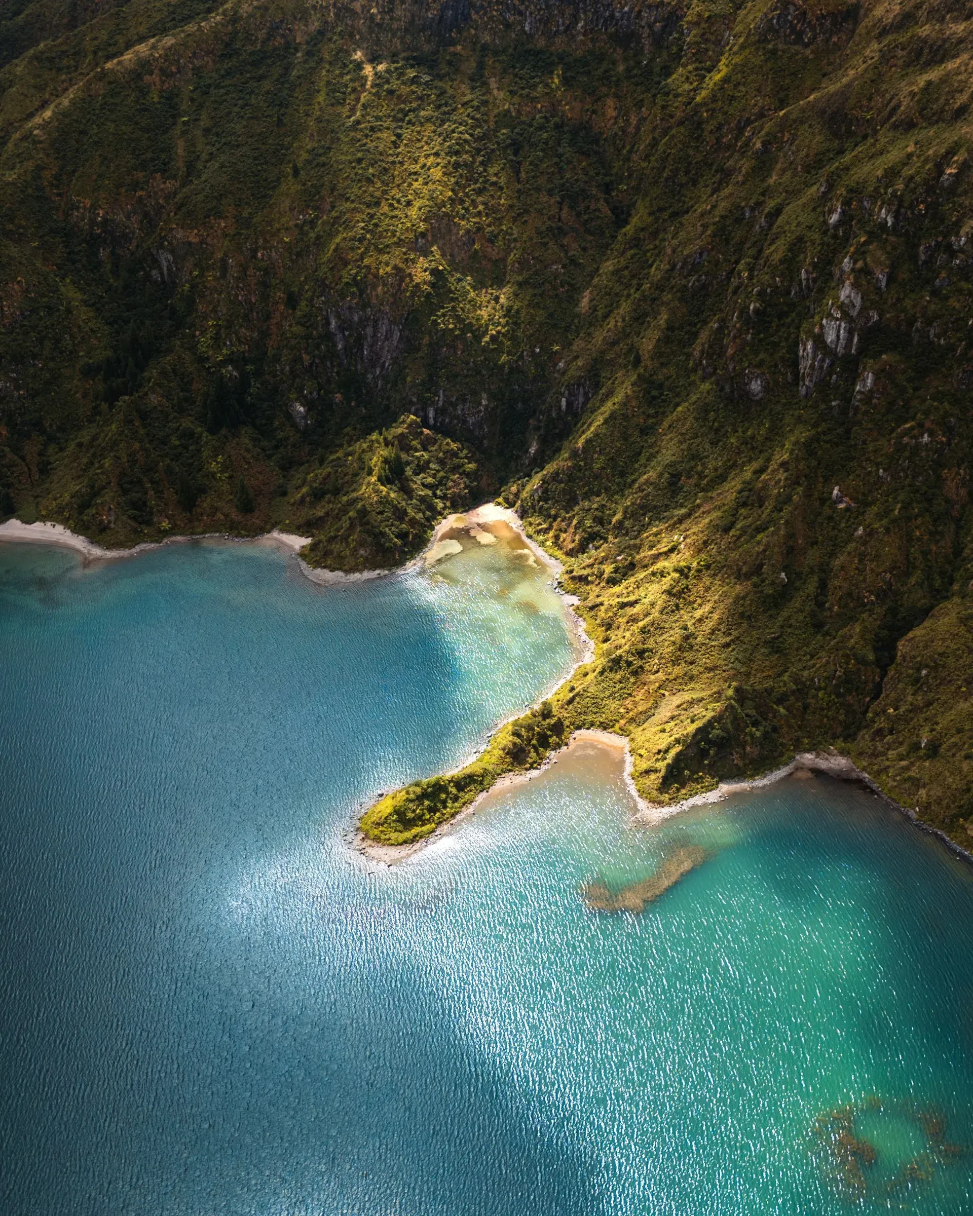 Close-up view of Lagoa do Fogo showing steep moss-covered crater walls and a narrow sandy beach along the shoreline
