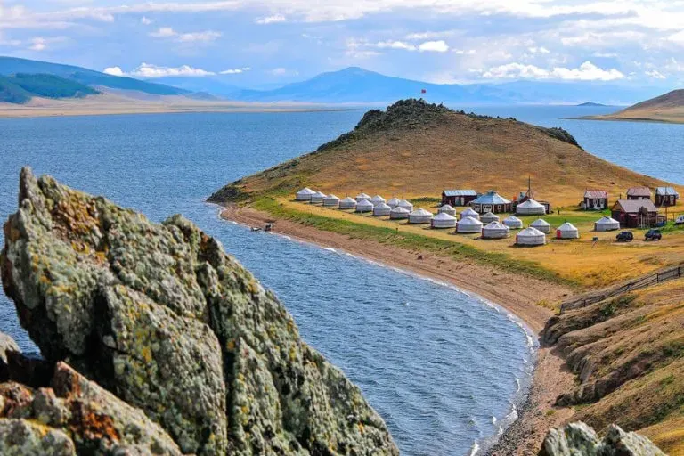 Traditional Mongolian gers on a grassy peninsula surrounded by blue waters