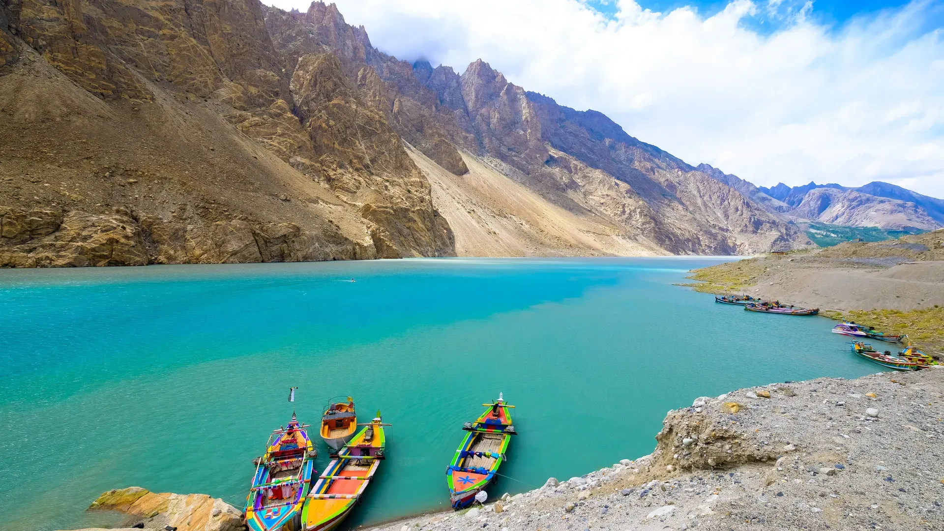 Traditional wooden boats anchored along the turquoise shoreline of Attabad Lake Pakistan in Hunza Valley