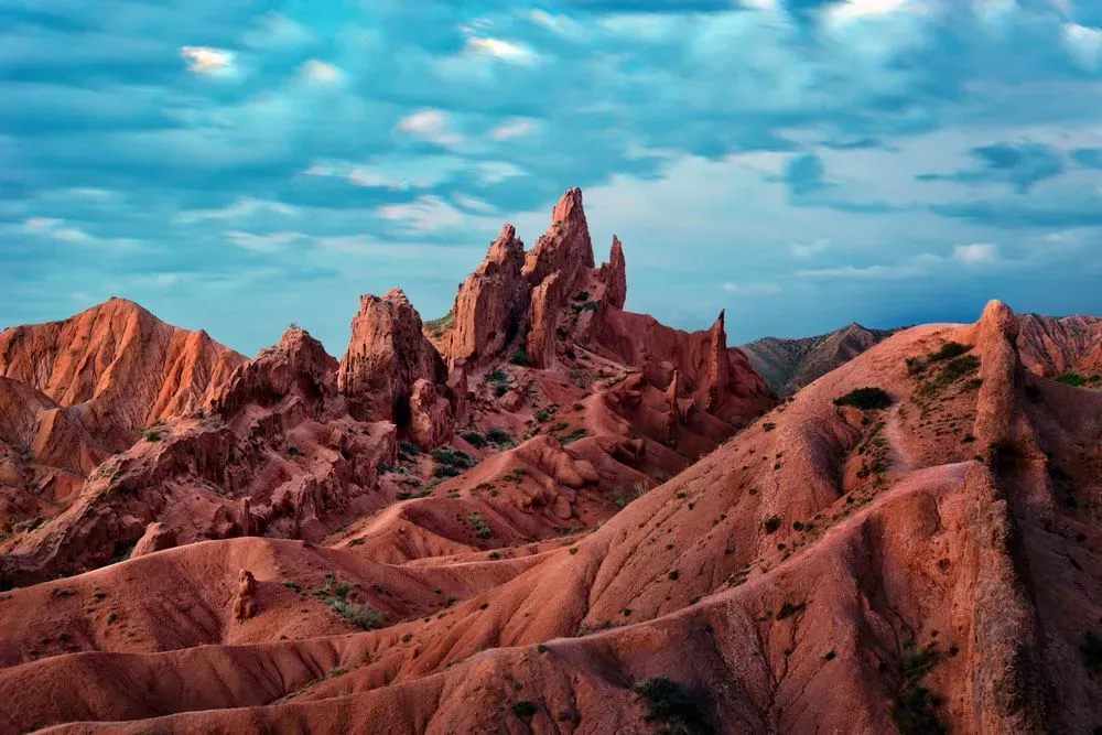 Wind-shaped red rock formations rising sharply against a partly cloudy sky in Skazka Canyon Kyrgyzstan