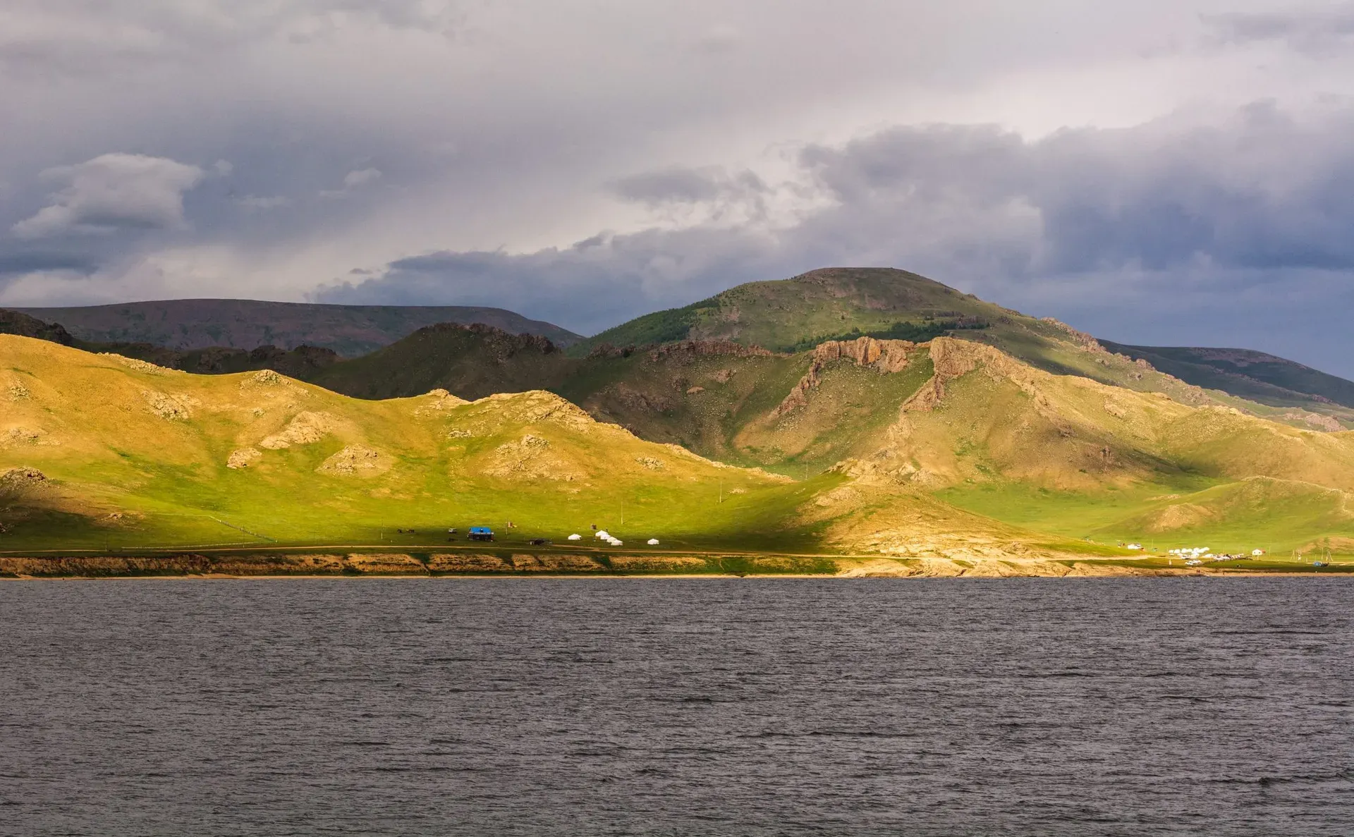 Expansive landscape of Terkhiin Tsagaan Lake with rolling green hills and black volcanic terrain