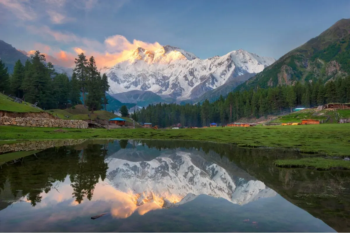 Golden sunset over Nanga Parbat with wooden houses and lake reflection