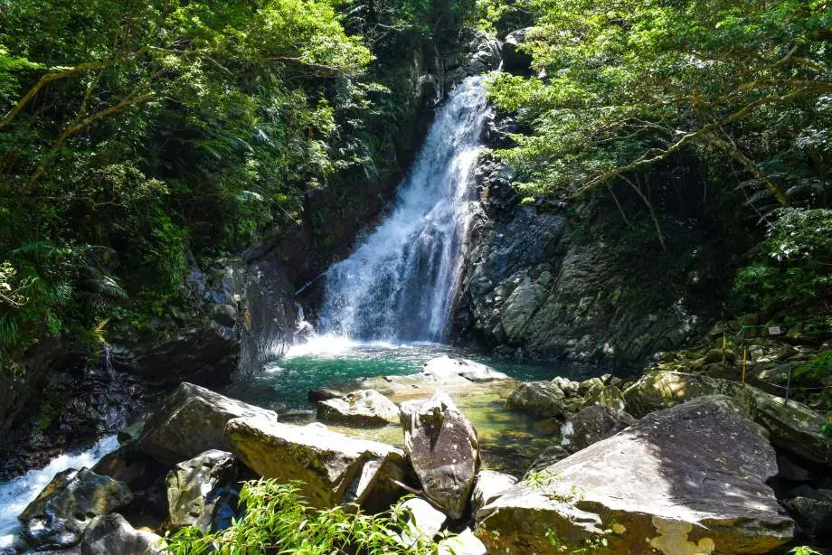 Hiji Falls waterfall cascading down rocky cliffs into a clear pool surrounded by lush greenery