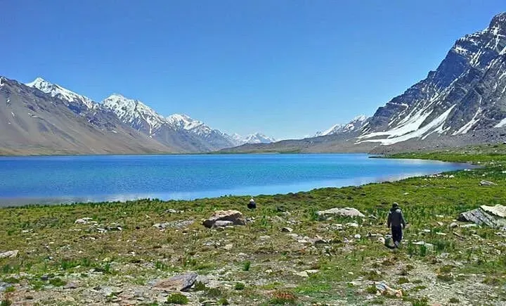 Hikers walking along the grassy shoreline of Karambar Lake