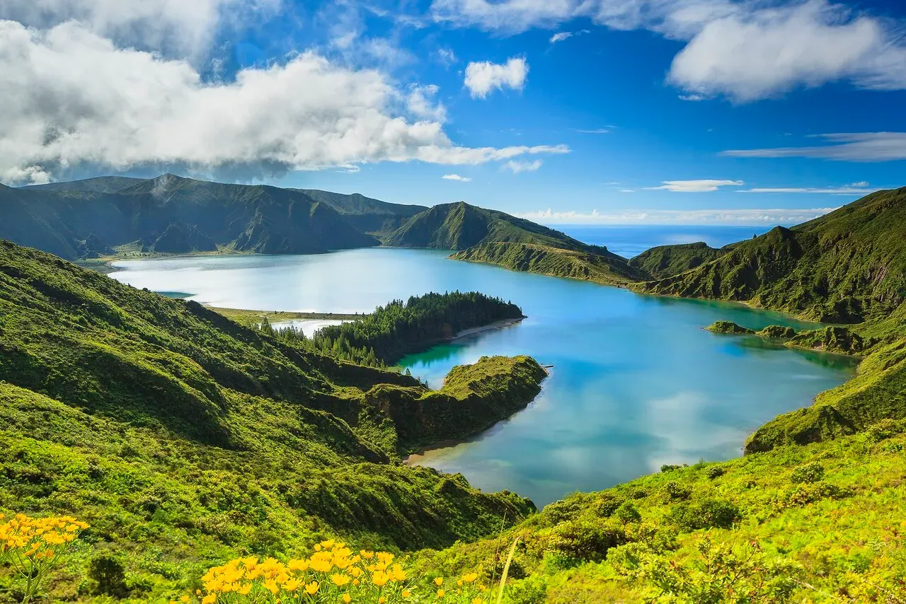 Lagoa do Fogo crater lake seen from above with dramatic clouds rolling over green hills and deep blue waters