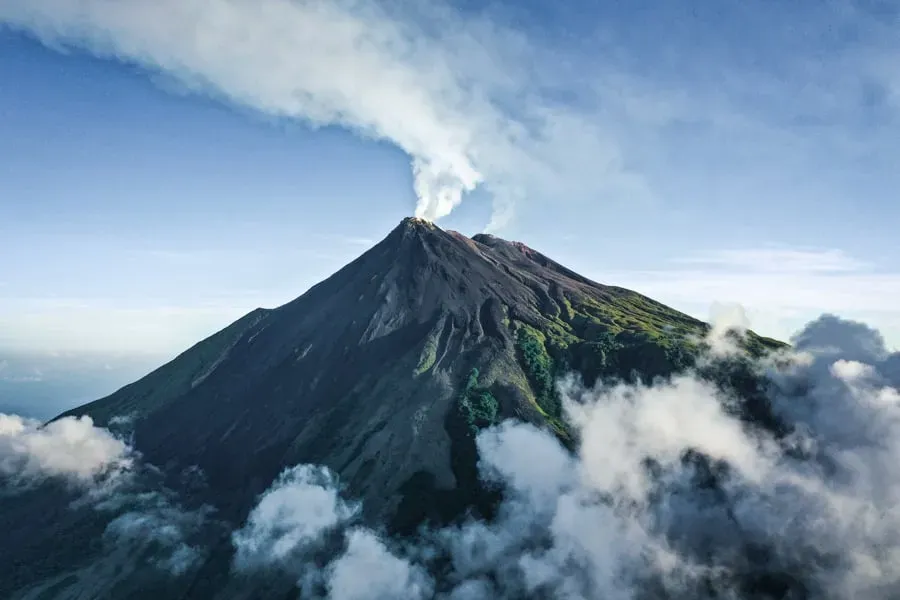 Mount Karangetang volcano crater smoking amid green slopes and drifting clouds on Siau Island, Indonesia