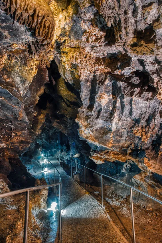 Narrow pathway with metal railings winding through illuminated stalactites and rock formations inside Grutas de Nombre de Dios Chihuahua