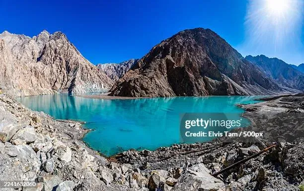 Panoramic view of Attabad Lake Pakistan turquoise water surrounded by rugged mountains under bright sunlight