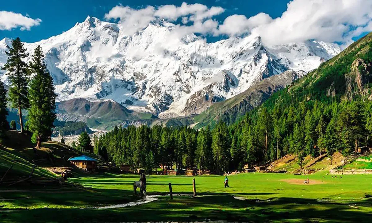 People riding horses across green meadow with Nanga Parbat backdrop