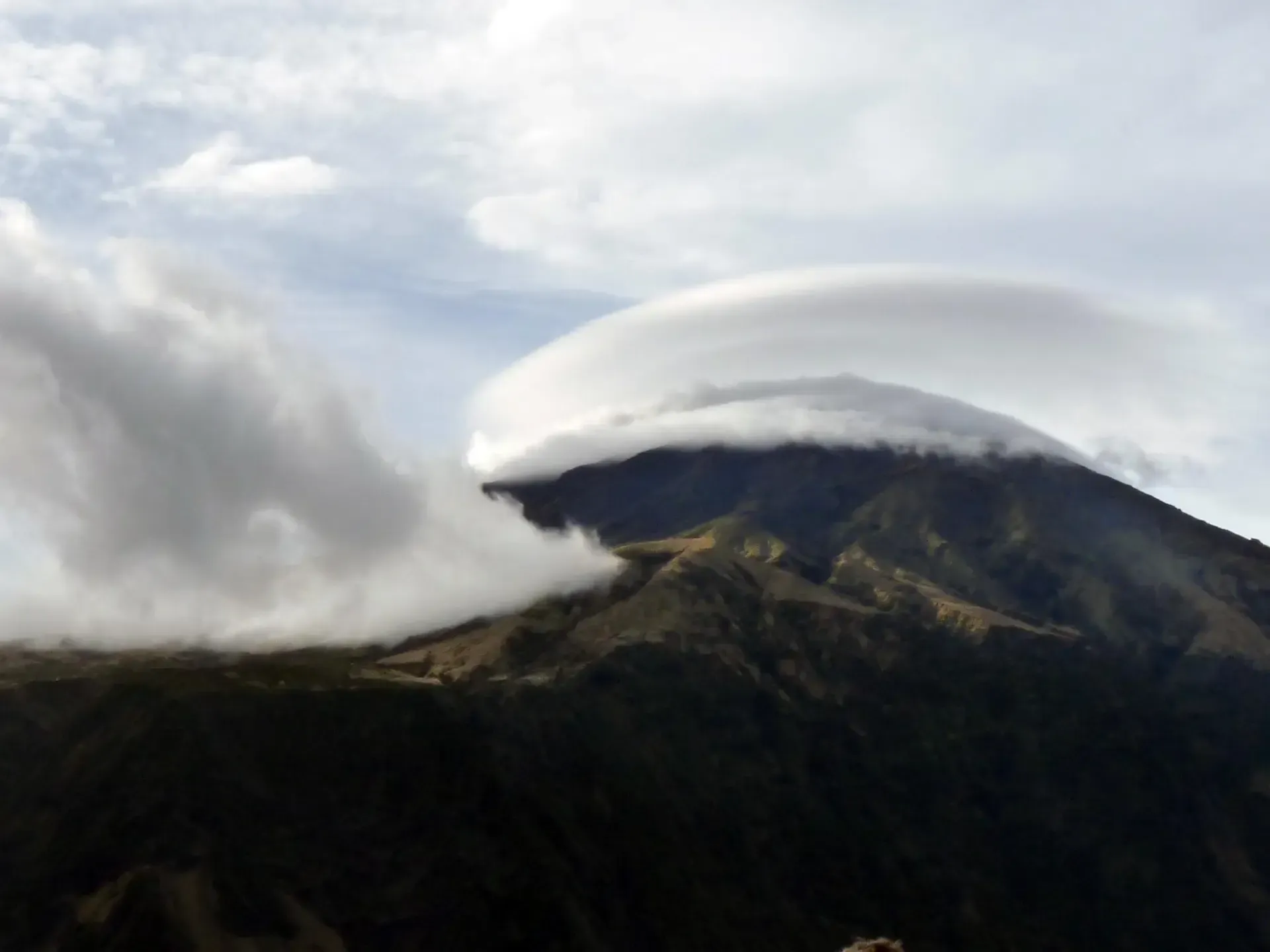 Queen Mary's Peak capped with clouds, with rugged volcanic terrain at its base