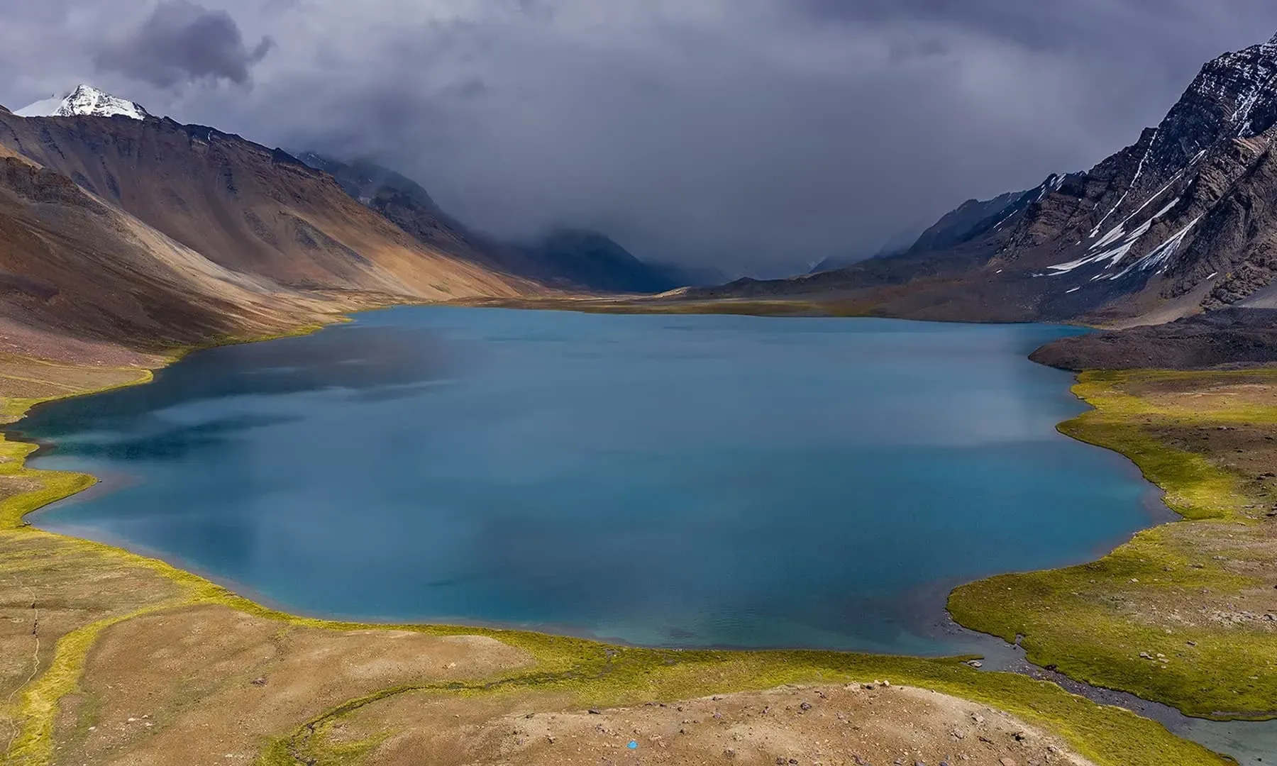 Karambar Lake Pakistan surrounded by grassy shores and snow-capped peaks