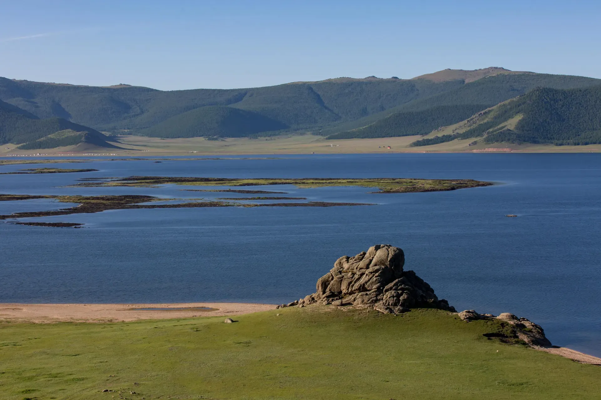 Serene shoreline of Terkhiin Tsagaan Lake with black volcanic rocks and clear turquoise water
