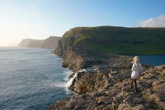Sunset at Bøsdalafossur with a person silhouetted against rocky cliffs and the Atlantic Ocean
